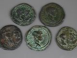 six pièces de monnaie romaines sont alignées sur une surface blanche