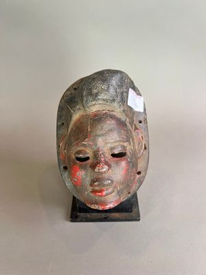 une image représentant un masque en bois posé sur un socle, sur une surface blanche