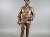 bronze statue of a man in uniform standing on a wooden base