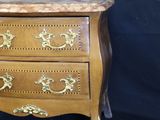 a small wooden chest of drawers with gold decorations