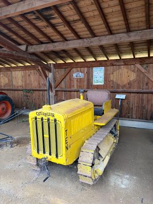 un tracteur jaune dans une grange, avec un autre tracteur derrière lui