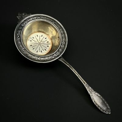 une cuillère en argent avec une passoire à l'intérieur, posée sur une surface noire