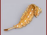 une image représentant une broche en forme de plume, en or et diamants