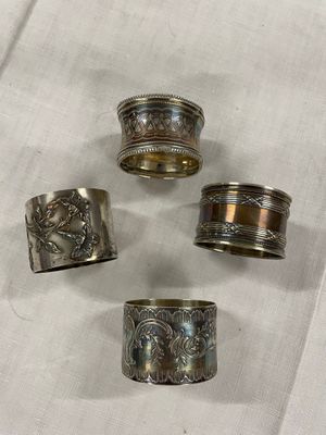 quatre ronds de serviette en argent ornés de motifs, posés sur une nappe blanche