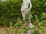 une statue représentant un homme assis sur un socle au milieu d'un jardin