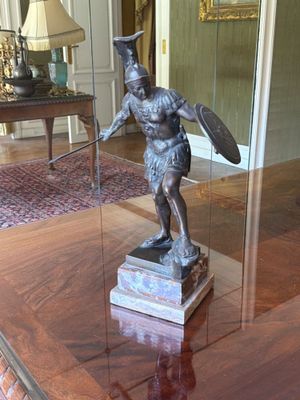 une statue représentant un homme tenant un bouclier, posée sur une table