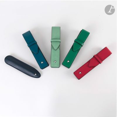 Quatre stylos en cuir de couleurs différentes sont alignés sur une surface blanche