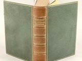 an old book with a green cover is open on a white surface