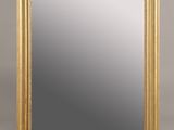 un miroir à cadre doré posé sur une surface blanche, avec un fond gris