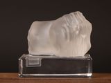 une sculpture blanche représentant un lion, posée sur un socle transparent