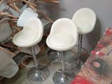 four white stools sitting in a room next to a pile of chairs