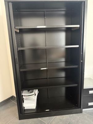 une bibliothèque en métal noir avec des tiroirs et des étagères dans une pièce