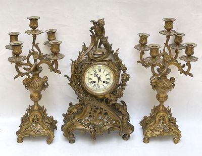 three gold colored candlesticks and a clock on a table