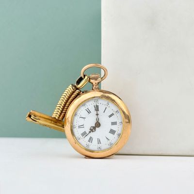 une montre de poche en or posée sur une table près d'un mur