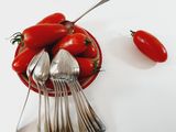 a bowl of tomatoes and spoons on a white table