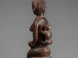 a wooden statue of a woman sitting on a stool