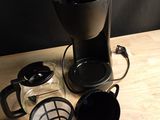 a black coffee maker and a glass cup on a wooden table