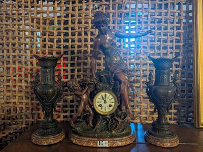 statue représentant une femme avec une horloge et deux vases posés sur une table