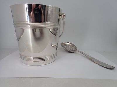 a silver ice bucket with a spoon and spoon on the table