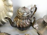 une théière en argent posée sur une table, à côté d'autres théières en argent
