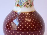 un vase rouge parsemé de points dorés sur un fond blanc