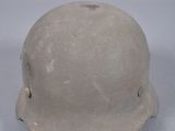 Un vieux casque repose sur une surface blanche, sur fond gris.