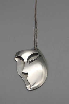 un masque en argent suspendu à une chaîne sur un mur blanc