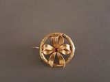 une image représentant une broche en forme de fleur en or, ornée d'une pierre rouge au centre