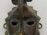 un masque antique en bronze surmonté d'un oiseau