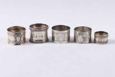six ronds de serviette en argent, ornés de motifs variés, posés sur un fond blanc