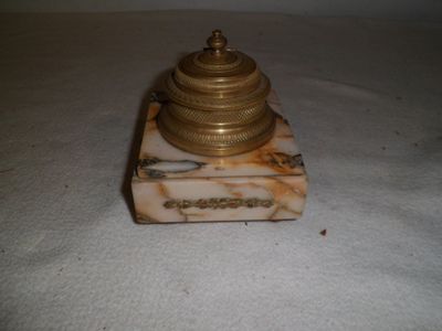 une petite horloge en or sur un socle en marbre sur une surface blanche