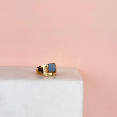 une bague en or et pierre bleue posée sur un bloc de marbre