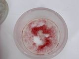 a red substance in a glass of water next to a coin