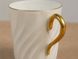 a white cup with a gold handle sitting on a table