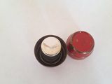 a small red jar with a white lid next to a small red jar with a white lid