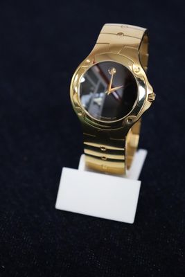 une montre en or avec un cadran noir posée sur un socle blanc