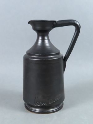 un vase noir muni d'une anse, posé sur une table