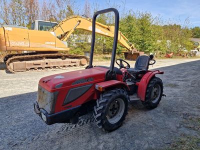 une photo d'un tracteur rouge garé sur un terrain en gravier