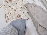 a pile of baby clothes and a hat on a bed