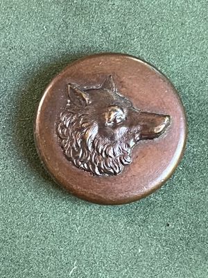 un badge en métal sur lequel est représenté un loup