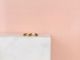 une alliance en or posée sur un bloc de marbre blanc, sur fond rose