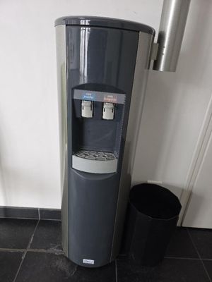 un distributeur d'eau posé par terre, à côté d'une poubelle