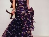 woman in a purple dress walking down a runway with a flower in her hair