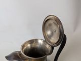 a small silver pitcher with a lid on a table
