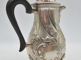 a silver coffee pot on a stand with a black handle