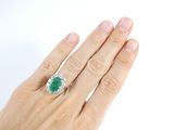 a woman ' s hand holding a ring with a green stone on it