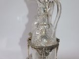 a glass bottle with a silver handle on a stand