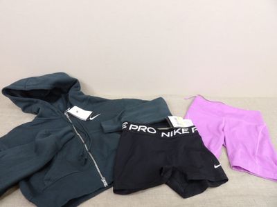 trois paires de shorts Nike et un sweat à capuche posés sur un lit