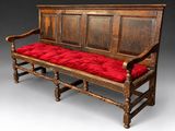 un banc en bois surmonté d'un coussin rouge, sur fond gris