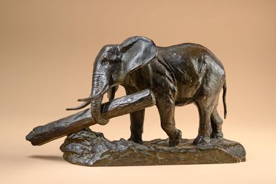statue of an elephant holding a log in its trunk on a beige background